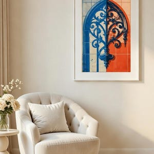 Puede incluir: Obra de arte enmarcada con un diseño simétrico en secciones azules y naranjas. La obra representa un elemento arquitectónico ornamentado y estilizado. El marco es blanco y la obra se exhibe sobre un sillón color crema con un cojín a juego.