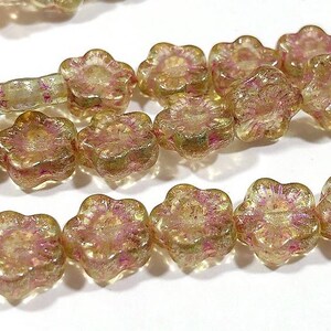 以下が含まれることがあります： 金とピンクの色合いの花の形をしたビーズのクローズアップ。 半透明のビーズは虹色の仕上がりです。 花柄は詳細で、各花びらが明確に定義されています。 これらのビーズは、ジュエリー作りに最適です。