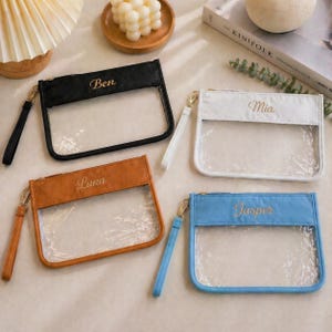 May include: Four personalized clear pouches with different colored tops: black with "Ben", white with "Mia", brown with "Luna", and blue with "Jasper". Each pouch has a gold zipper and a matching wrist strap.