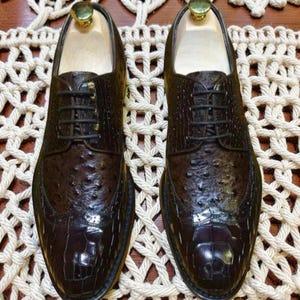 May include: A pair of dark brown leather dress shoes with a textured, patterned design. The shoes have a classic lace-up style and a polished finish. The image shows the shoes from a top-down perspective, highlighting their intricate details.