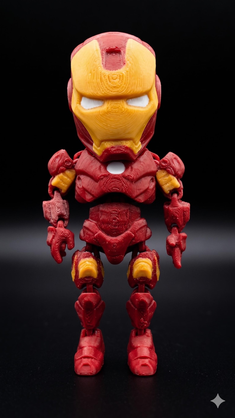 May include: A 3D-printed Iron Man figurine in a standing pose. The figure is primarily red with yellow accents on the helmet and joints. The eyes are white. The background is solid black.
