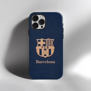 May include: A navy blue phone case featuring the FC Barcelona crest in gold. The crest includes a cross, stripes, and a soccer ball. The word "Barcelona" is printed below the crest in gold.