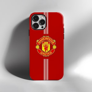 May include: Red phone case with white vertical stripes and the Manchester United logo. The logo is in a circular design with the words "Manchester United" and a crest with a ship and a devil.