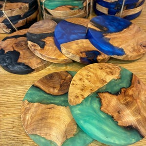 May include: A collection of handcrafted wooden coasters with epoxy resin accents. The coasters feature natural wood grain patterns and are available in various colors, including black, blue, and green. Each coaster is approximately 4 inches in diameter.
