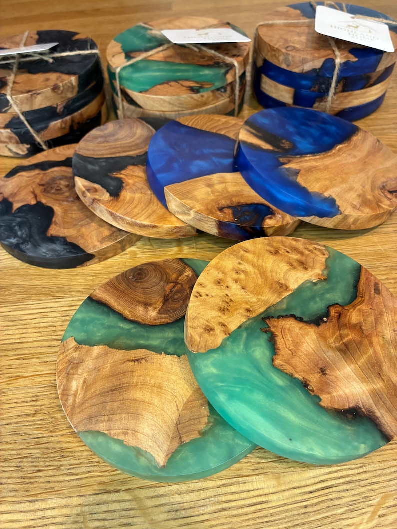 May include: A collection of handcrafted wooden coasters with epoxy resin accents. The coasters feature natural wood grain patterns and are available in various colors, including black, blue, and green. Each coaster is approximately 4 inches in diameter.