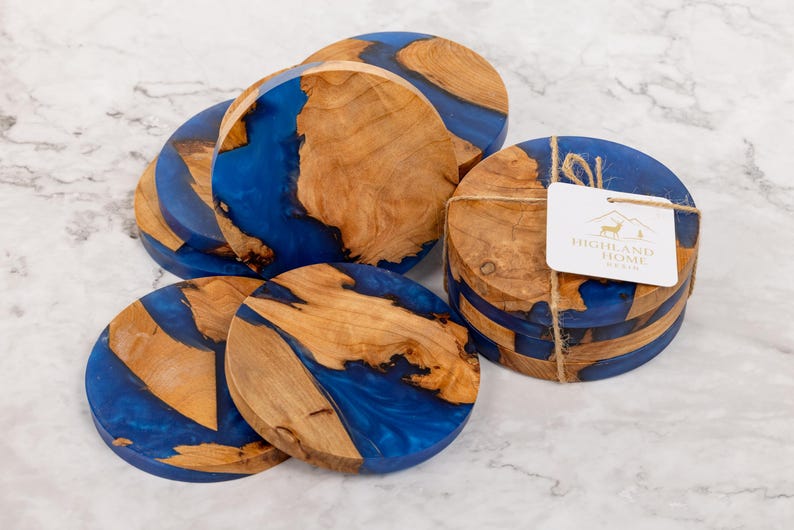 May include: Set of round wooden coasters with a blue resin inlay. The coasters have a natural wood grain pattern and are bundled together with twine. A tag with the words "Highland Home" is attached.