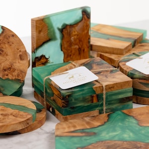 May include: A collection of handcrafted wooden coasters and blocks with a unique design. The coasters and blocks feature a combination of natural wood and teal-colored resin, creating a striking contrast. Some are round, others square.