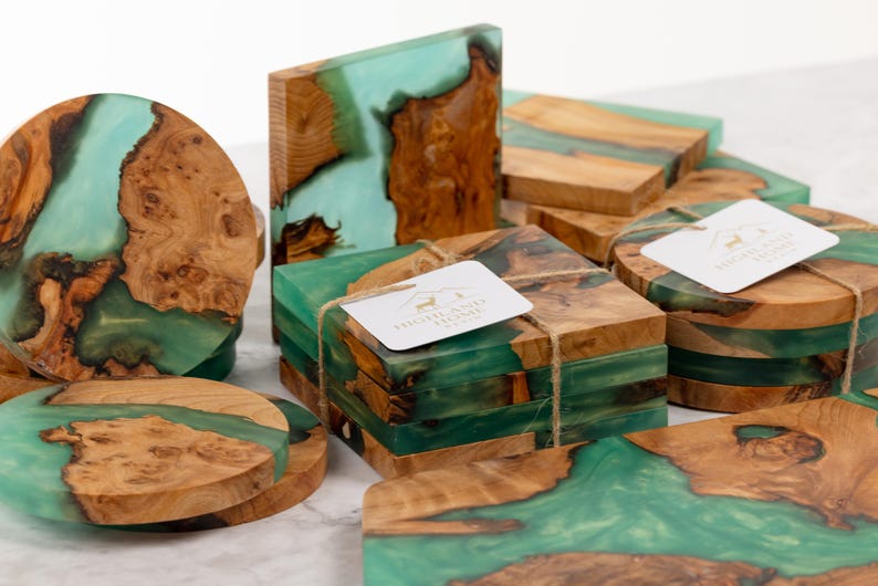 May include: A collection of handcrafted wooden coasters and blocks with a unique design. The coasters and blocks feature a combination of natural wood and teal-colored resin, creating a striking contrast. Some are round, others square.