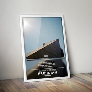 Puede incluir: Un póster enmarcado con la portada del álbum "Freudian" de Daniel Caesar. La imagen muestra a una persona en el tejado de un edificio contra un cielo azul. El póster incluye una lista de canciones y el título del álbum en texto blanco.