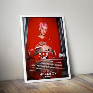May include: A framed poster featuring Lil Peep in a red jersey with "New Jersey Devils" text. The poster has a red background and includes the album title "Hellboy" and a tracklist. The image is leaning against a wooden surface.