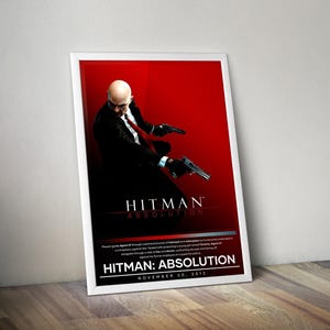 Puede incluir: Póster enmarcado del videojuego "Hitman: Absolution". Muestra a un hombre calvo con traje negro y corbata roja, sosteniendo dos pistolas sobre un fondo rojo. El título del juego se muestra de forma destacada.