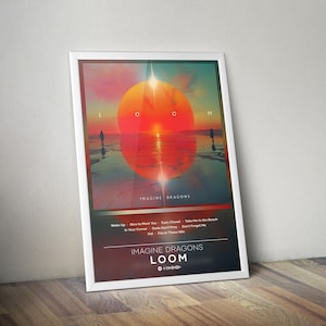 Puede incluir: Un póster enmarcado con una escena de puesta de sol, con un gran sol naranja y siluetas. El póster incluye el texto "IMAGINE DRAGONS" y "LOOM", además de una lista de títulos de canciones. El marco es blanco.