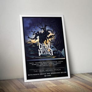 May include: A framed poster featuring the band "The Devil Wears Prada." The artwork depicts a dark, gnarled tree against a moody, blue-toned background. The band's name is prominently displayed in a stylized font, with song titles listed below.