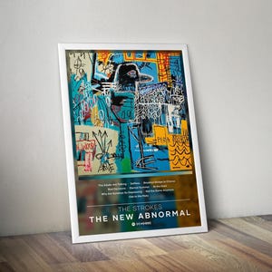 May include: A framed art print with an abstract design in blue, yellow, and white. The print displays the band name "THE STROKES" and album title "THE NEW ABNORMAL". The print is propped against a wooden floor.