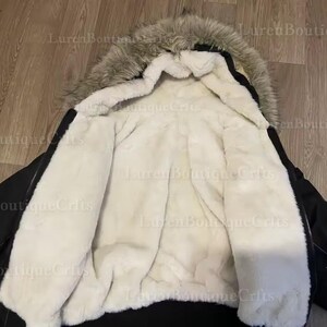 May include: Black winter coat with a faux fur-lined hood and a cream-colored, plush interior. The coat's exterior is a solid black, and the hood features a mix of gray and brown faux fur.