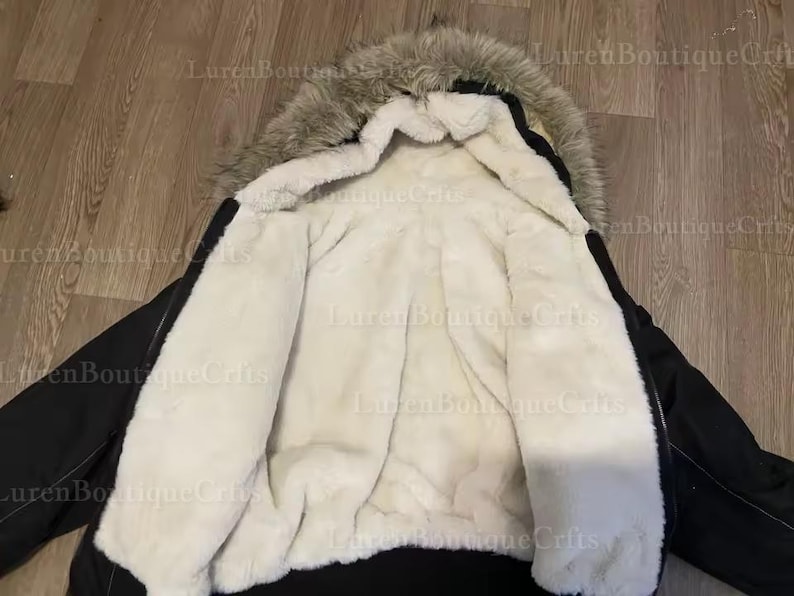 May include: Black winter coat with a faux fur-lined hood and a cream-colored, plush interior. The coat's exterior is a solid black, and the hood features a mix of gray and brown faux fur.