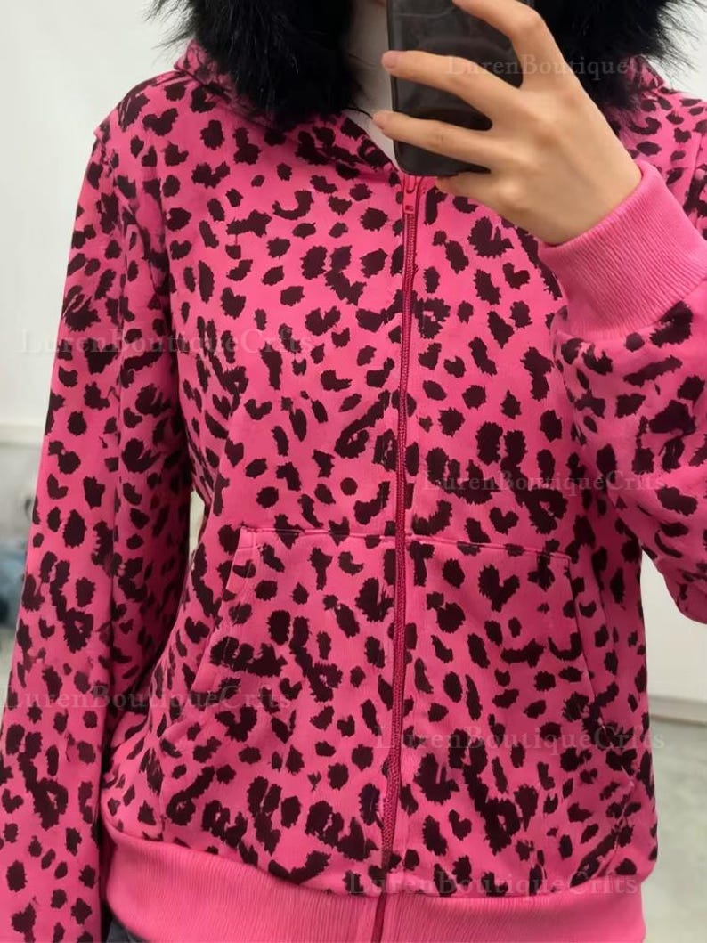 Puede incluir: Una sudadera con capucha rosa con cremallera y estampado de leopardo negro. La sudadera tiene una capucha forrada de piel sint&eacute;tica negra, una cremallera frontal y dos bolsillos delanteros. Los pu&ntilde;os y el dobladillo son de color rosa liso.