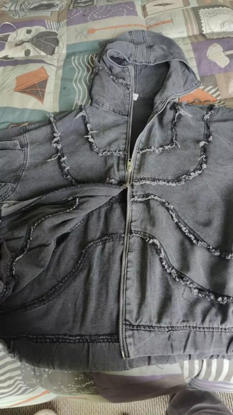 Puede incluir: Chaqueta con capucha de mezclilla gris con cierre de cremallera. La chaqueta presenta bordes deshilachados decorativos a lo largo de las costuras y alrededor de la capucha. La chaqueta es de mezclilla suave.