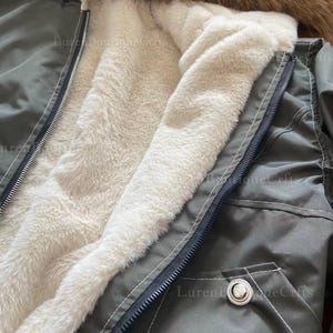 May include: Close-up of an olive green winter coat with a cream-colored, fluffy interior lining. The coat features a black zipper, a buttoned pocket, and a brown fur-lined hood. The image highlights the coat's warm and cozy design.