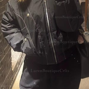 May include: Black bomber jacket with a fur-trimmed hood and white stitching details. The jacket features a zipper closure and two front pockets. The pants are black with decorative studs. The image has the text "Luren Boutique Crfts".