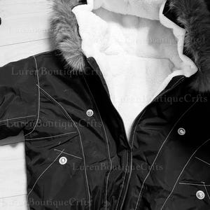 May include: Black bomber jacket with a faux fur-trimmed hood and white interior lining. The jacket features a zipper closure, pockets, and white stitching details. The jacket is a winter outerwear garment.