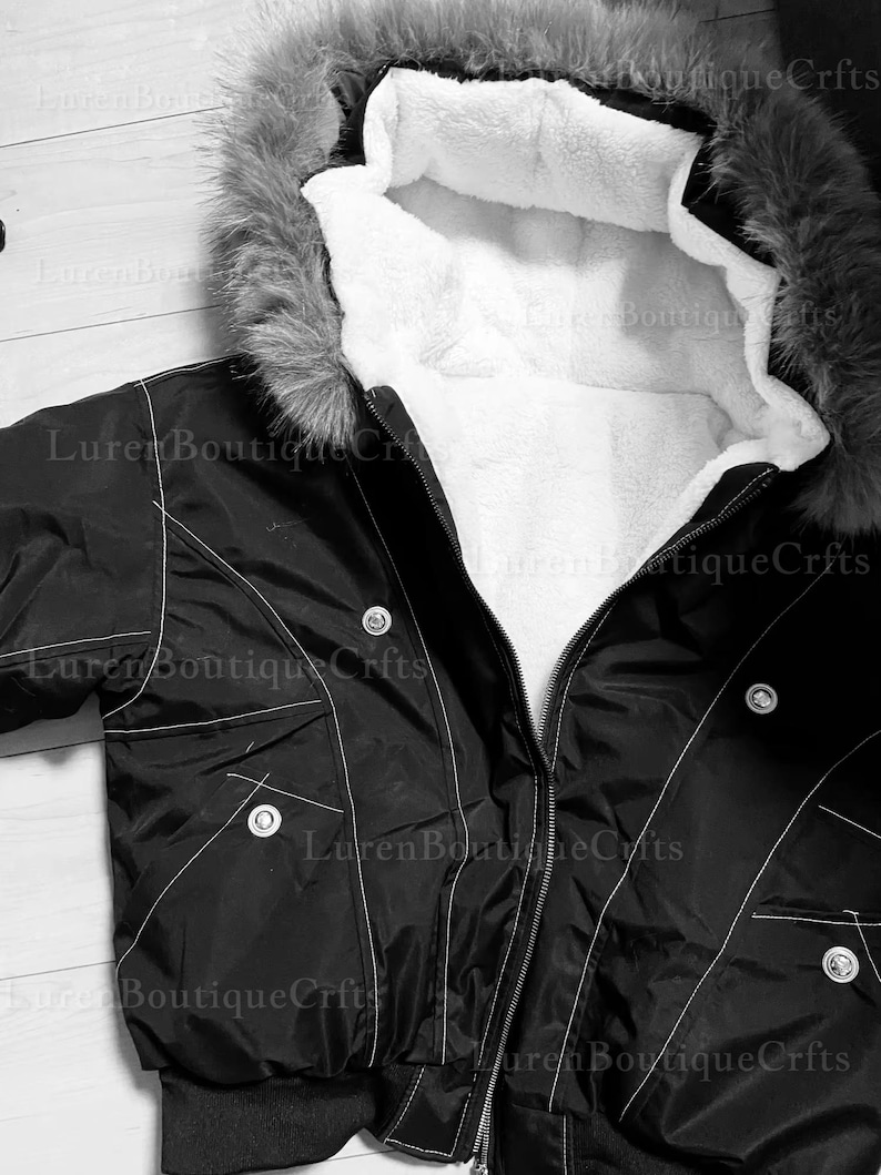May include: Black bomber jacket with a faux fur-trimmed hood and white interior lining. The jacket features a zipper closure, pockets, and white stitching details. The jacket is a winter outerwear garment.