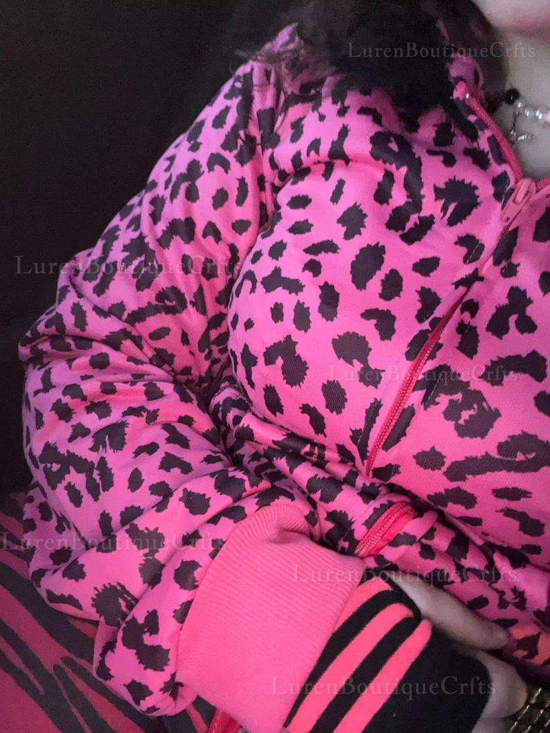 Puede incluir: Una chaqueta rosa brillante con un estampado de leopardo negro. La chaqueta tiene cierre de cremallera y pu&ntilde;os de canal&eacute; rosas con rayas negras. La chaqueta forma parte de un conjunto a juego.