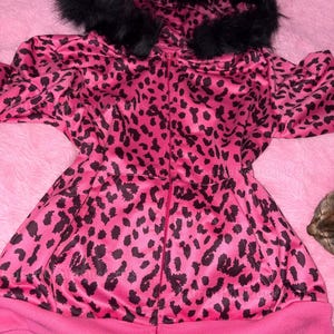 Puede incluir: Chaqueta rosa con cremallera y estampado de leopardo negro. La chaqueta tiene una capucha forrada de piel sint&eacute;tica negra y un dobladillo y pu&ntilde;os de canal&eacute; rosa. La chaqueta est&aacute; hecha de un material brillante.