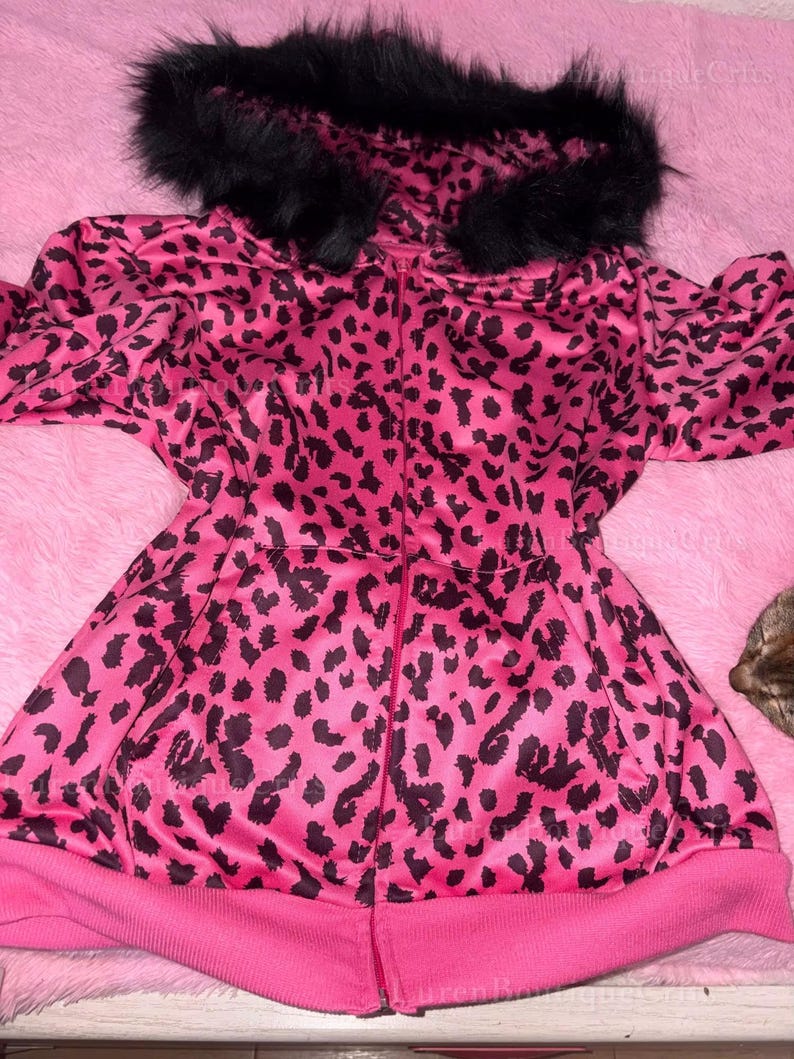 Puede incluir: Chaqueta rosa con cremallera y estampado de leopardo negro. La chaqueta tiene una capucha forrada de piel sint&eacute;tica negra y un dobladillo y pu&ntilde;os de canal&eacute; rosa. La chaqueta est&aacute; hecha de un material brillante.