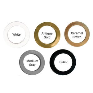 May include: Five circular curtain grommets arranged in a group. Each ring features a distinct color and a label in the center: White, Antique Gold, Caramel Brown, Medium Gray, and Black. The rings have a smooth, flat surface and a circular opening.