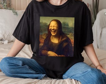 May include: Black t-shirt featuring a humorous image of the Mona Lisa laughing. The image is a parody of the famous painting, with the subject's face contorted in laughter. The shirt is a casual style, suitable for everyday wear.