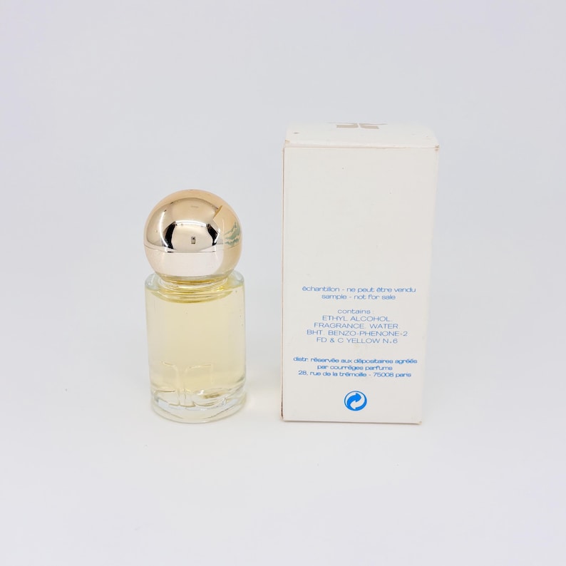 May include: A clear glass perfume bottle with a gold-colored cap and a white box. The bottle contains a light yellow liquid. The box has text that reads "sample - not for sale".