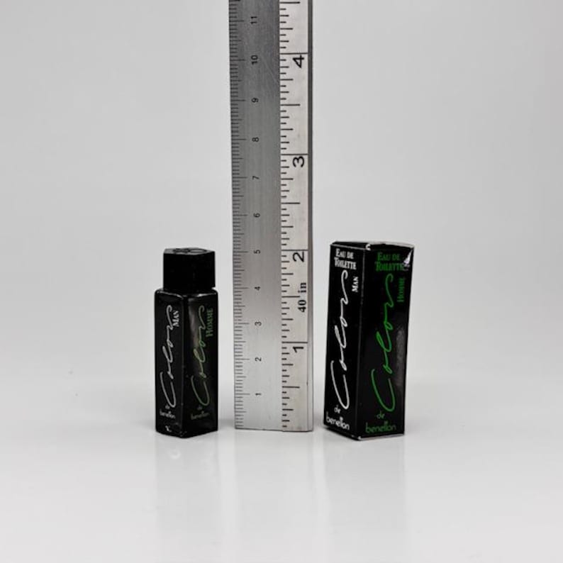 May include: A black perfume bottle and box with the text "Colors Man Homme" in green and white. The bottle is approximately 2 inches tall, and the box is about 3 inches tall. A metal ruler is next to the perfume.
