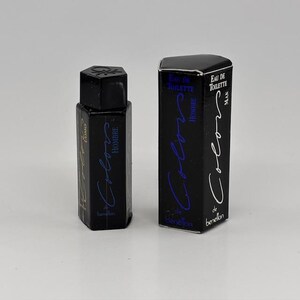 May include: A black hexagonal perfume bottle and matching box. The bottle and box feature the text "Colors de Benetton Hombre" in blue and white script. The bottle has a black cap and the box reads "Eau de Toilette Man".