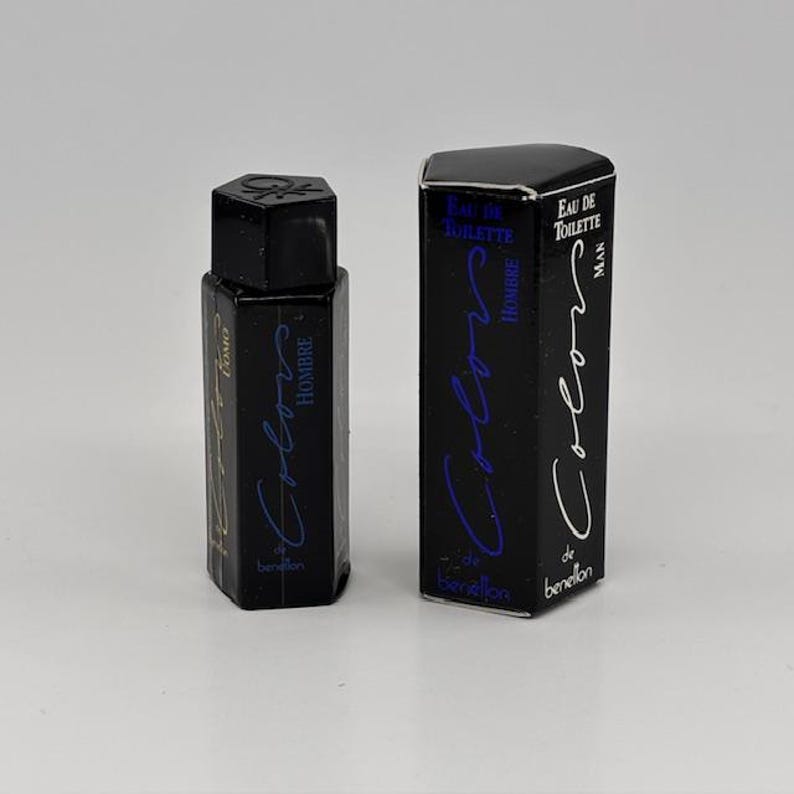 May include: A black hexagonal perfume bottle and matching box. The bottle and box feature the text "Colors de Benetton Hombre" in blue and white script. The bottle has a black cap and the box reads "Eau de Toilette Man".