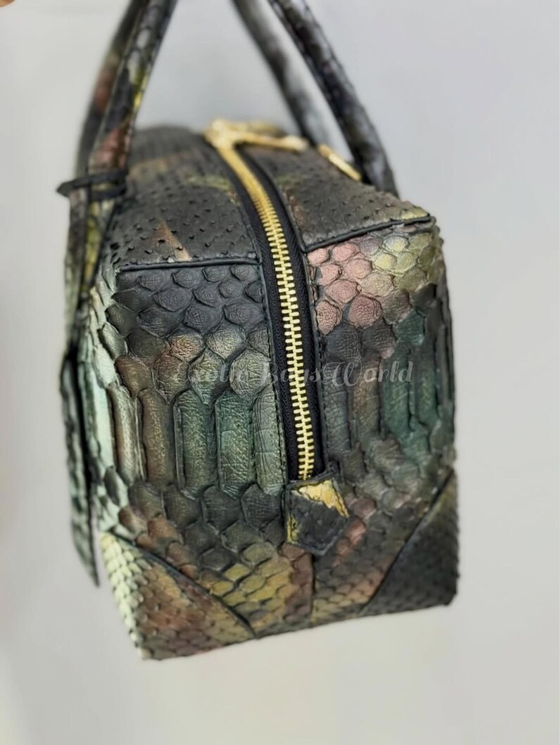 May include: A rectangular handbag with a camouflage pattern in shades of green, brown, and gold. The bag features a gold zip and handles. The texture of the bag appears to be snakeskin.