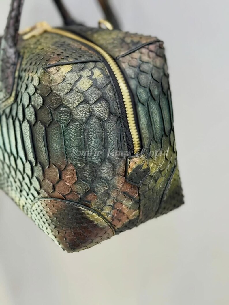 May include: A close-up of a textured, multi-coloured handbag. The bag features a zip closure and a braided handle. The colours include shades of green, brown, and gold, creating a unique, eye-catching design.