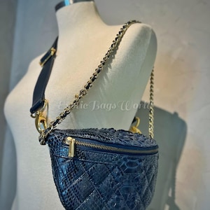 Può includere: Un marsupio in pelle trapuntata blu navy con cerniera dorata e tracolla a catena. La borsa è esposta su un manichino. La tracolla è una combinazione di pelle e catena dorata. La borsa ha un motivo a rombi.