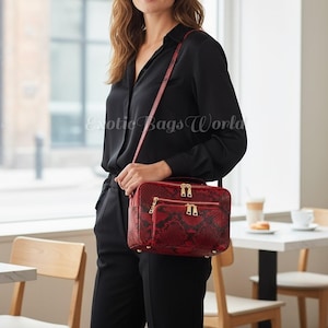 May include: A red snakeskin-patterned crossbody bag with gold zippers and hardware. The bag has a rectangular shape with two zippered compartments. The bag is worn over the shoulder with a matching red strap. The text "Exotic Bags World" is visible.