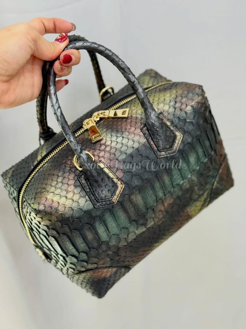 May include: A multi-coloured handbag with a snakeskin pattern. The bag has a rectangular shape, a top zip, and two handles. Gold-coloured hardware accents the bag, including the zip and handle attachments. The bag's colours include green, brown, and gold.