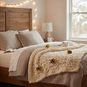 May include: A cozy bedroom scene featuring a wooden bed frame and headboard. The bed is adorned with neutral-toned bedding and a chunky cream-colored blanket decorated with bee-shaped embellishments. A string of lights hangs above the bed.