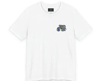 May include: White t-shirt featuring a small embroidered design of a gray elephant playing with a colorful ball. The shirt has a classic crew neck and short sleeves. The elephant design is on the left chest area.