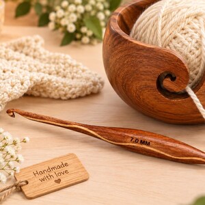 Può includere: Un uncinetto in legno levigato con una marcatura di misura 7.0 mm, accompagnato da una ciotola per filati in legno abbinata contenente un gomitolo di lana color crema e una piccola etichetta rettangolare in legno incisa con Handmade with love.