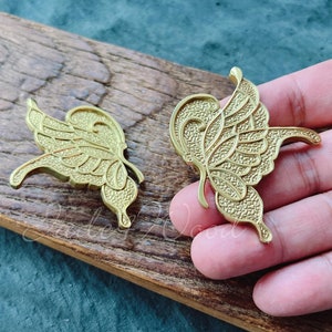 Puede incluir: Dos tiradores de cajón de metal dorado en forma de mariposa con detalles intrincados.