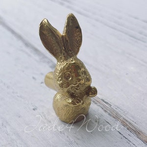 May include: A gold-colored rabbit figurine with a detailed design. The rabbit is sitting upright with its ears perked up and its eyes open. The figurine is made of metal and has a smooth finish.