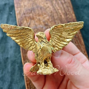 Op de afbeelding: Een gouden adelaarfiguur met uitgespreide vleugels. De adelaar staat op een kleine basis en heeft een gedetailleerd ontwerp.