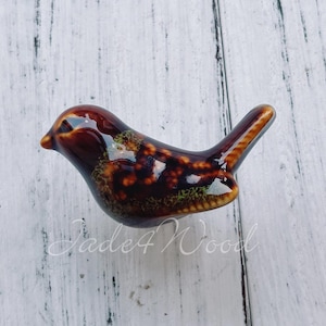 Peut inclure: Une figurine d'oiseau en céramique avec un glaçage moucheté brun et noir. L'oiseau a une longue queue et un petit bec.