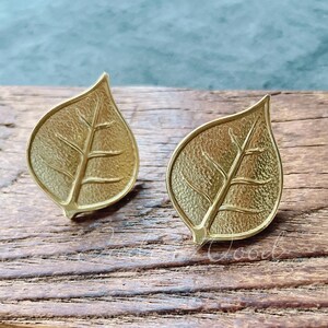 May include: A pair of gold leaf-shaped earrings. The earrings are made of metal and have a textured surface.
