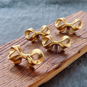 Peut inclure: Quatre poignées de tiroir en métal doré en forme de nœud sur une surface en bois.