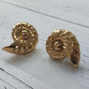 Peut inclure: Une paire de boucles d'oreilles dorées en forme de coquillages. Les boucles d'oreilles sont détaillées avec un motif en spirale et ont une finition lisse et polie.